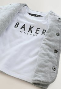 Hallidega kardigan, millel on nupuklõpsud, on kihiliselt seljas valge T-särk, millel on must tekst "BAKER" ja "by TED BAKER." Pehme puuvillane kangas.