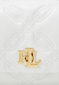 Bílá kožená kabelka s embosovaným vzorem řetězů, zlatou sponou s logem "RL" a kontrastním bílým prošíváním. Elegantní a moderní design.