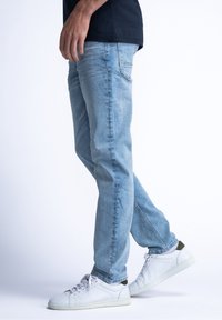 Vaqueros de mezclilla azul claro con diseño de pierna recta, textura desgastada y dos bolsillos traseros, combinados con zapatillas blancas.