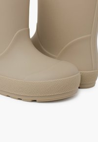Bottines de pluie en caoutchouc beige avec une finition lisse, bout rond et semelle texturée pour une bonne adhérence. Design à couper bas avec des accents minimalistes.