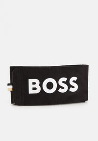 Portefeuille en suède noir avec un audacieux logo "BOSS" blanc. Comprend une accent en or et noir rayé sur le côté. Forme rectangulaire plate.