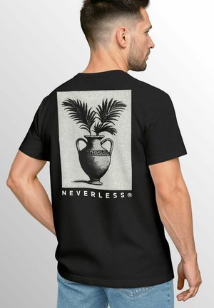 A man stands with his back to the viewer, wearing a black t-shirt featuring a decorative vase with palm leaves and the text "NEVERLESS."