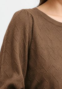 Braun gemusterter Pullover mit einem strukturierten, diamantähnlichen Design. Verfügt über einen runden Ausschnitt und leicht gepuffte Ärmel aus einem weichen Material.