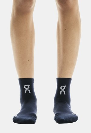 Chaussettes de cheville bleu marine en tissu texturé, avec un logo blanc sur chaque chaussette et un design uni. Bord-côte tricoté à la cheville pour un maintien ajusté.