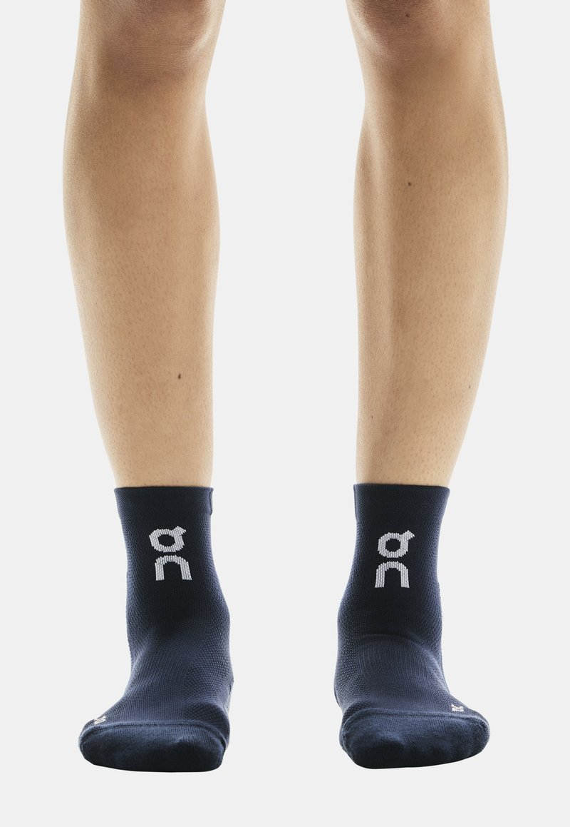 Chaussettes de cheville bleu marine en tissu texturé, avec un logo blanc sur chaque chaussette et un design uni. Bord-côte tricoté à la cheville pour un maintien ajusté.