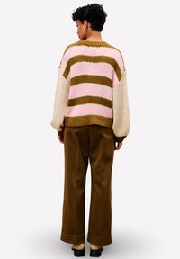 Gestickter Pullover mit pinken, braunen und cremefarbenen Streifen; lockere Passform, überschnittene Schultern. Braune weit geschnittene Hose mit hochgekrempeltem Saum; getragen mit schwarzen Schuhen.