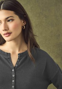 Chemise henley gris foncé avec un col rond, cinq boutons sur le devant et des manches longues. Texture lisse, coupe décontractée.