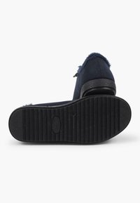 Scarpe slip-on in suede blu navy con suola in gomma nera testurizzata e bordo in morbido pellicciotto attorno all'apertura. Design con tacco piatto e dettagli minimi.