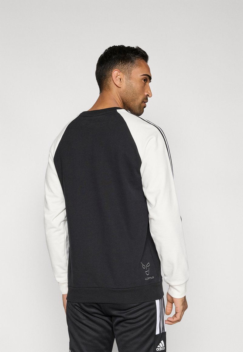 Schwarz-weißes Sweatshirt mit Raglanärmeln, Rundhalsausschnitt und Logodetail in der Nähe des Saums. Der Stoff wirkt glatt und leicht strukturiert.