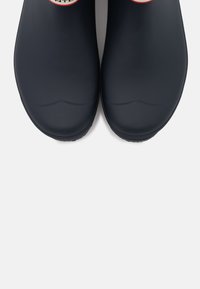 Sabots en caoutchouc bleu marine avec une finition lisse, un orteil arrondi et une semelle texturée. Présente un logo circulaire sur la partie supérieure de chaque chaussure.