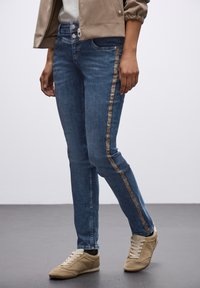 Jeans de mezclilla azul claro con pierna recta, que presentan una franja de estampado de leopardo a lo largo del costado, combinados con zapatillas beige.