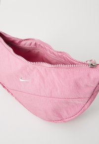 Rosa Nylon Tasche mit strukturierter Oberfläche, geschwungener Form, Metallreißverschluss und einem kleinen silbernen Logo. Geöffnet, um den Innenraum zu zeigen.