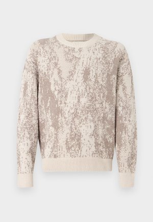 Pleteni pulover u krem i bež boji s teksturiranim, apstraktnim uzorkom. Ima okrugli izrez i rebraste manžete i rub.