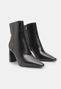 Black leather ankle boots with a pointed toe, block heel, and side zipper. Smooth texture with a sleek design and minimal detailing.