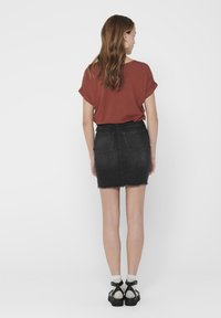 Top rosso a maniche corte, mini gonna di jeans nera con orlo sfilacciato e sandali neri con calzini bianchi. Focus su tessuto e design informale.