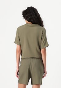 Olive green short-sleeve jumpsuit with a relaxed fit, featuring an elastic waistband and smooth fabric, designed for comfort and ease of movement.
