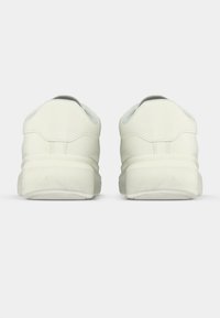 Scarpe da ginnastica bianche con tomaia in pelle liscia, tallone arrotondato e suola testurizzata. Design minimalista con dettagli di cuciture sottili.