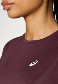 Camiseta deportiva en color marrón, de mangas cortas y cuello redondo, con un pequeño logotipo blanco en el pecho, hecha de una tela suave y ligera.