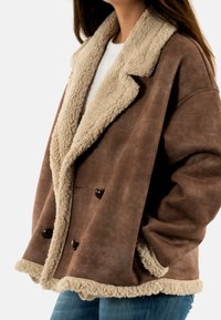 Abrigo de mezcla de lana marrón con un cuello y forro de pelaje sintético beige, diseño de doble botón, con grandes botones oscuros y un ajuste relajado.