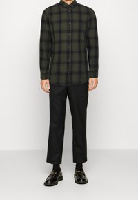 Groen en zwart geruit overhemd met een kraag, gecombineerd met zwarte broek en zwarte instappers met een gouden kettingaccent.