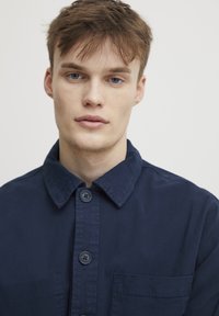 Navy blue shirt made of cotton, featuring a spread collar, two-button front closure, and a chest pocket. Smooth texture with subtle sheen.
