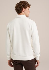 Sudadera blanca con cuello, textura suave, puños y dobladillo acanalados. Diseño simple sin patrones. Modelo visto por detrás.
