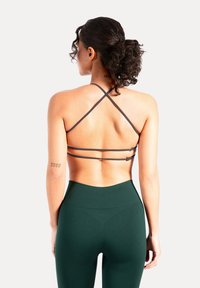 Vista trasera de un sujetador deportivo gris oscuro con tirantes cruzados, combinado con leggings de tiro alto en verde oscuro. Tejido liso, diseño minimalista.