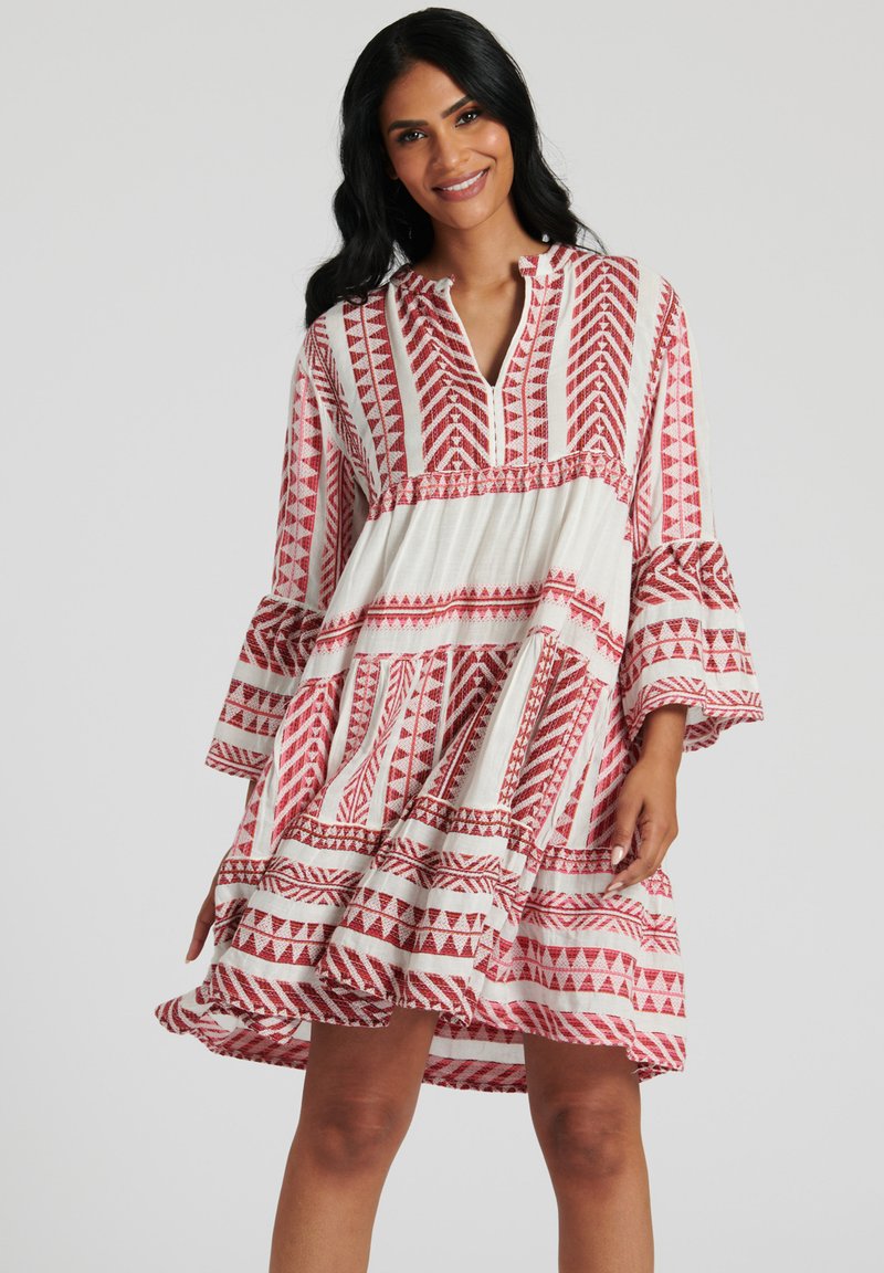 Röd och vit mönstrad klänning med v-ringning, långa utsvängda ärmar, lagerdesign och geometriska motiv genom hela plagget. Lätt, texturerad tyg.