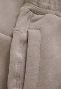 Beige bomullstyg med en slät textur. Har ribbade ärmslut och en sidoficka med synlig s�ömnad och sömdetaljer.