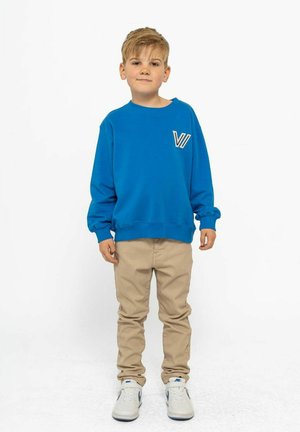 Blauwe sweatshirt met een zakaccent, beige broek en witte sneakers. De sweatshirt heeft een ronde halslijn en lange mouwen.