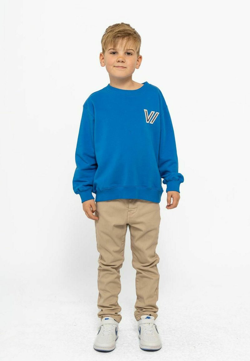 Blå sweatshirt med en fickdetalj, beige byxor och vita sneakers. Sweatshirten har rundad hals och långa ärmar.