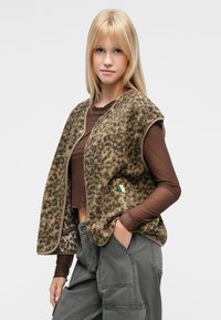Γιλέκο από φλις με σχέδιο λεοπάρ σε αποχρώσεις του καφέ, με κούμπωμα με κουμπιά, στρογγυλή λαιμόκοψη και πλαϊνές τσέπες. Συνδυάζεται με γκρι παντελόνι cargo.