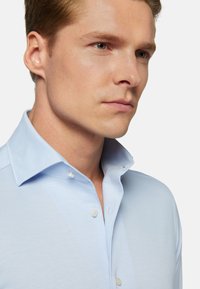 Svetlomodrá košeľa s gombíkmi vyrobená z mäkkej tkaniny, s špicatým golierom, jemnou textúrou a dvoma gombíkmi viditeľnými na krku.