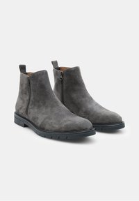 Stivali alla caviglia in suede grigio con cerniere laterali, punte arrotondate e suole in gomma con scanalature per una migliore trazione. Texture liscia e design minimalista.