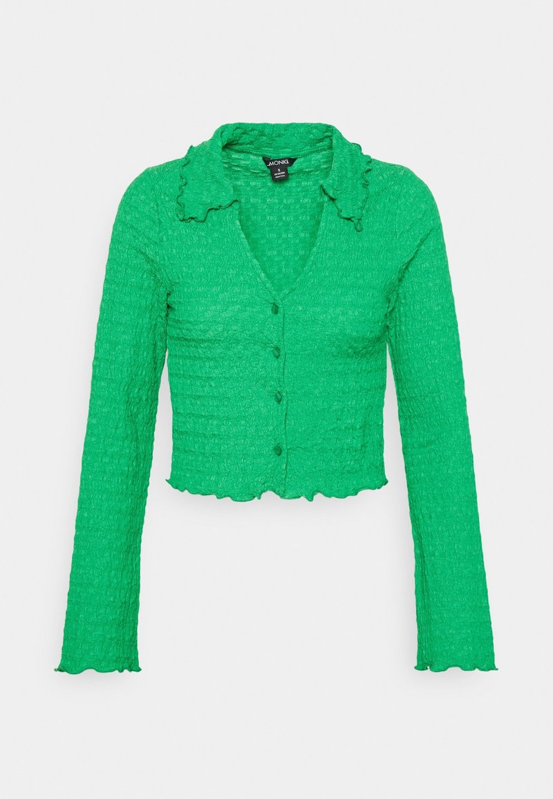 Cárdigan verde corto con un tejido texturizado y arrugado, mangas largas, escote en V y bordes del cuello con volantes, que cuenta con cinco botones en la parte delantera.