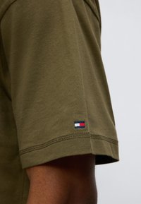 Πράσινο χακί βαμβακερό μπλουζάκι με κοντά μανίκια, που διαθέτει ένα μικρό κεντημένο λογότυπο σε κόκκινο, λευκό και μπλε στη ραφή του μανικιού.