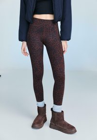 Hnědé legíny s leopardím vzorem a vysokým pasem, doplněné o hnědé semišové boty do kotníku a světle modré manžetové ponožky.