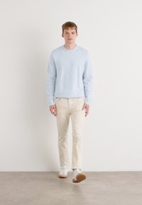 Lichtblauwe trui, crèmekleurige chinos en witte sneakers. De trui heeft een ronde halslijn. Glad textuur en casual pasvorm.