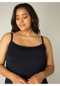 Zwarte tanktop met dunne bandjes. Glad, rekbaar materiaal. Ronde halslijn. Strakke pasvorm die een comfortabele uitstraling toont.