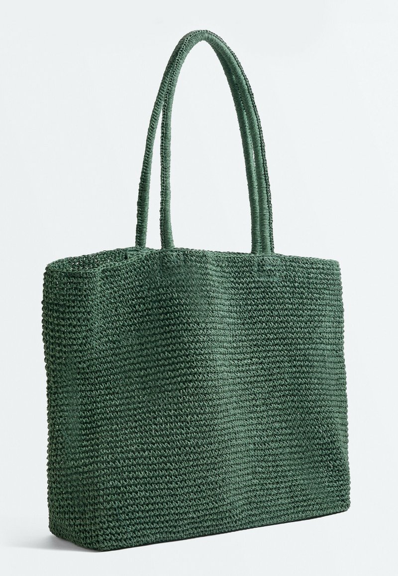 Sac cabas tissé vert foncé avec deux poignées de longueur moyenne, forme rectangulaire et surface texturée, debout.