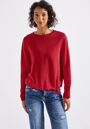 Roter Sweatshirt mit langen Ärmeln, rundem Halsausschnitt, gerafftem Kordelzugsaum und glatter Textur, kombiniert mit hellblauen, strukturierten Jeans.