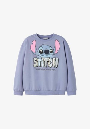 Lilla genser med stor Stitch-tegneserie som holder glitrende "STITCH"-tekst og mottoet "vær god, vær glad, vær quirky, vær deg" under.