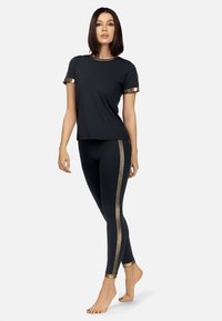 Czarna sportowa bluzka z złotymi akcentami i rękawami, w zestawie z czarnymi legginsami z złotymi paskami po bokach. Gładki materiał z dopasowanym krojem.