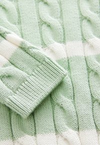 Knit sweater featuring alternating light green and cream stripes, with textured cable patterns and ribbed cuff details. Soft cotton blend material.