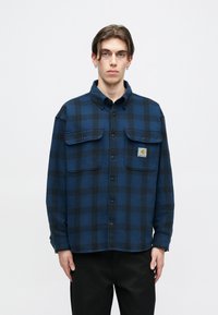 Μπλε και μαύρο καρό φανελένιο πουκάμισο με γιακά που κουμπώνει, δύο τσέπες στο στήθος και μία μικρή λογότυπη ετικέτα στη αριστερή πλευρά.