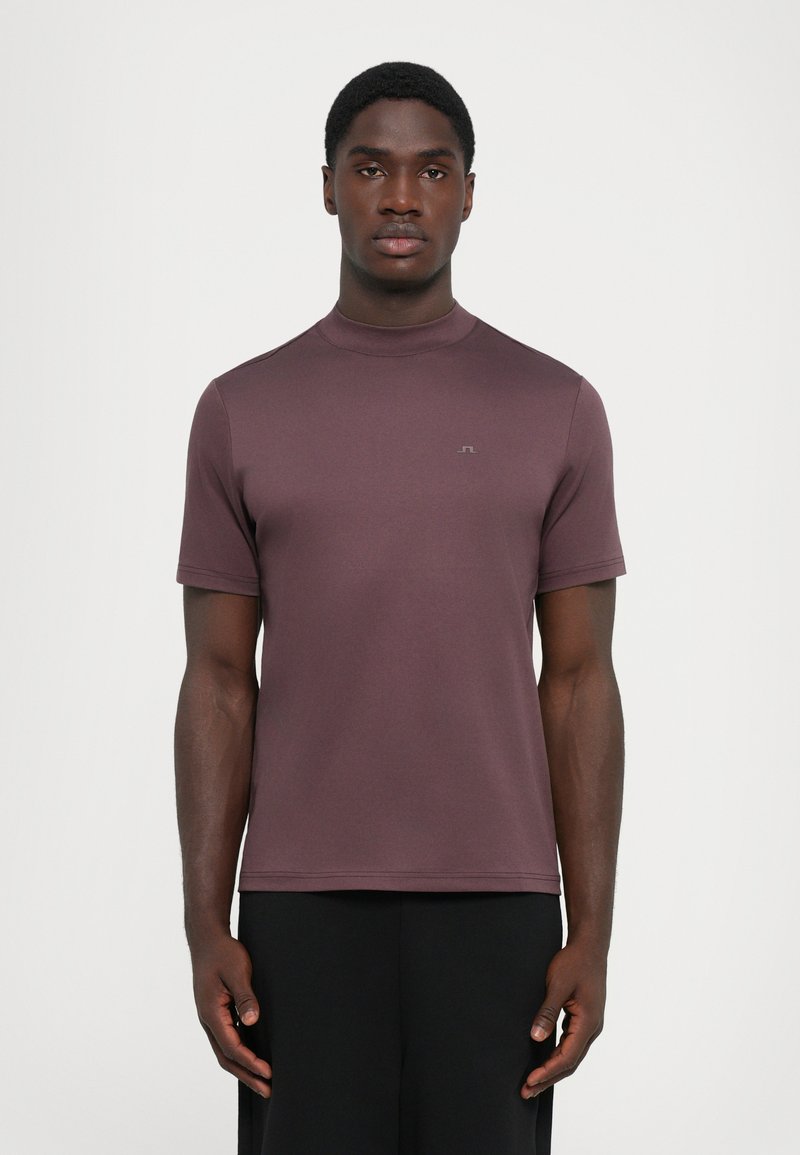 Kortermet skjorte i dempet mauve, laget av mykt stoff med høy halsdesign. Har et minimalistisk logo på brystet og en jevn tekstur.