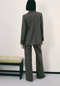 Traje de lana gris texturizada con un blazer a medida y pantalones de pierna ancha. Incluye detalles de botones y un diseño simple, visto desde atrás.