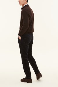 Tummanruskea neulottu paita kauluksella, yhdistettynä tummiin corduroy-housuihin ja ruskeisiin mokkanahkaisiin loafereihin, nähtynä sivulta.