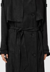 Svart trenchcoat med midjebälte, dubbelknäppning och en något oversize passform. Slät textur och minimalistiska designdetaljer.