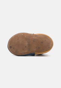 Sole di scarpa in suede con una base marrone chiaro, caratterizzata da una superficie testurizzata e motivi a stella in argento. Curva semplice e dettaglio blu sul bordo.